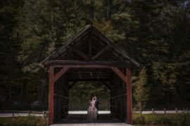 A bride and groom enjoying a summer wedding at Riverside Farm, standing in front of a covered bridge.