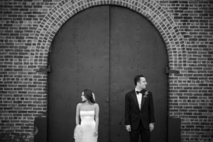 A wedding couple in New York, standing elegantly in front of a brick door.