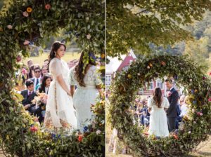 A summer wedding at Riverside Farm, with a bride and groom standing in front of a wreath of flowers.