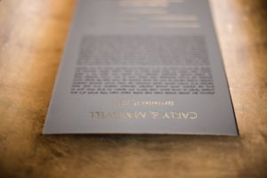 A black and gold wedding program on a wooden table in New York.