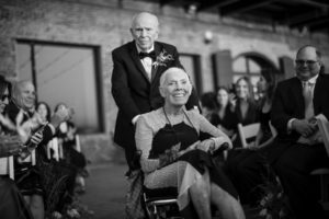 A man in a wheelchair is being wheeled down the aisle at a wedding in New York.