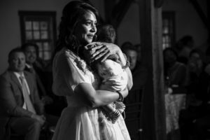 A woman is holding a baby at a summer wedding ceremony.