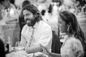 A black and white photo of a man smiling at a summer wedding.