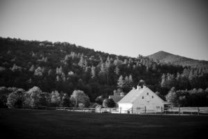 A black and white photo of a white barn in the mountains, showcasing Riverside Farm's scenic beauty.