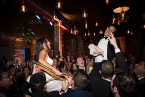 A bride and groom being carried by a group of people at a New York wedding.