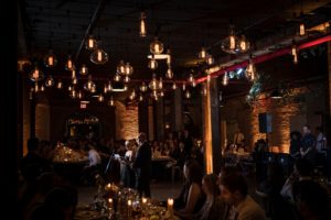 A wedding reception in a warehouse with lights hanging from the ceiling in New York.
