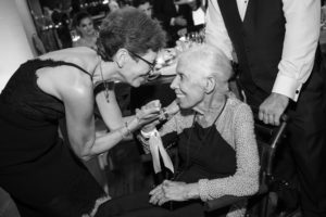 A woman in a wheelchair is giving a woman a piece of cake at a wedding.