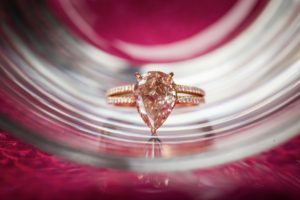 An engagement ring with a pear shaped diamond sits on top of a glass, perfect for a New York wedding.