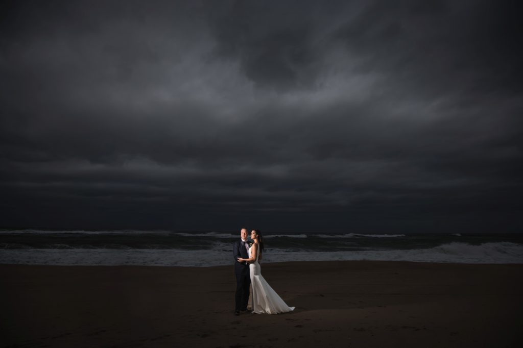 A wedding couple standing on the beach under a stormy sky in New York.