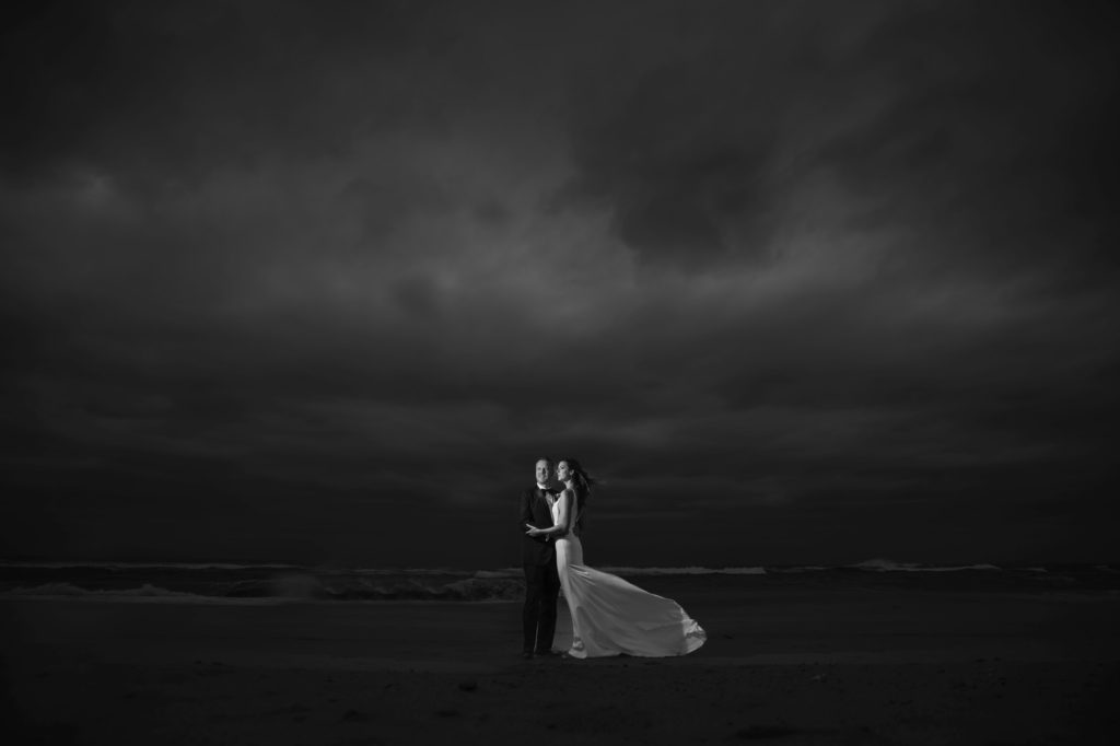 A bride and groom standing on the beach under a stormy sky in New York for their wedding.