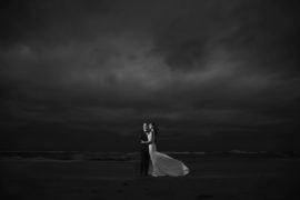 A bride and groom standing on the beach under a stormy sky in New York for their wedding.