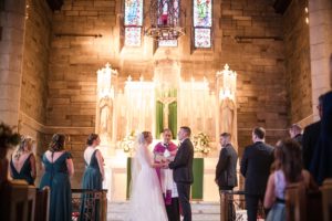 A bride and groom standing in front of a stained glass window on their wedding day in New York.