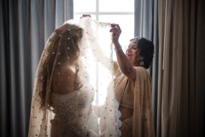 A bride getting ready for her wedding day in New York, carefully placing her veil in front of a window.