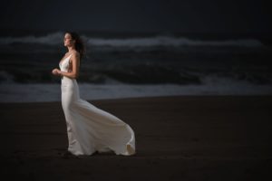 A bride in a white wedding dress standing on the beach at night in New York.
