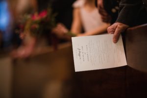 A person holding a wedding program in front of a pew at a wedding in New York.