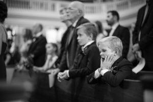 A little boy is sitting in the pews at a wedding ceremony in New York.