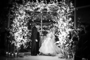 A bride and groom standing under an arch decorated with flowers at their New York wedding.