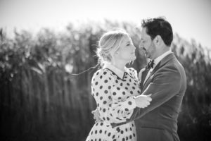 A black and white wedding photo of a couple hugging in front of tall grass in New York.