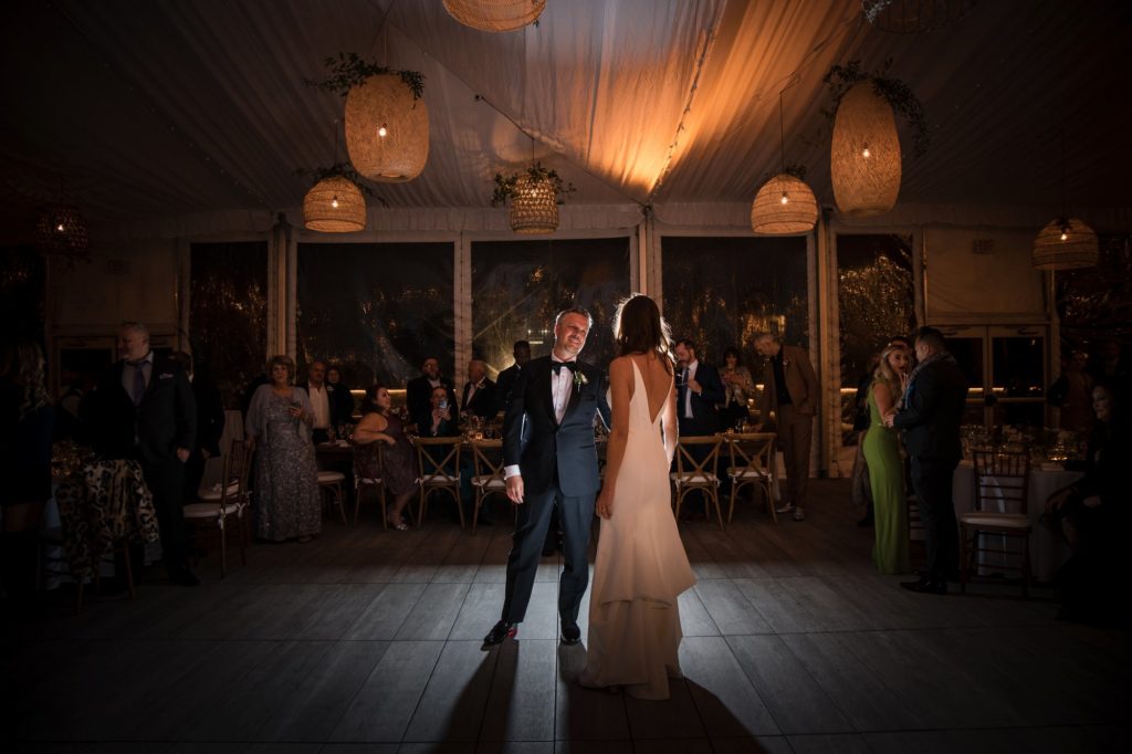 In the enchanting ambiance of a tent nestled amidst the vibrant cityscape of New York, a bride and groom share an intimate dance on their wedding night.