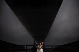 A new york bride and groom standing under a bridge under a cloudy sky on their wedding day.