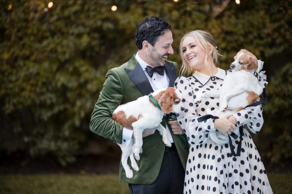 A man and woman in polka dot tuxedo holding two dogs at their wedding in New York.