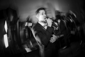 A man in a suit singing into a microphone at a wedding in New York.