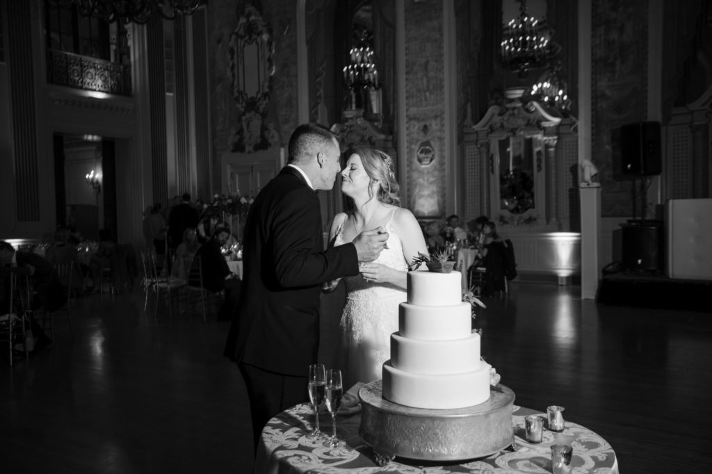 A bride and groom passionately kissing in front of a large cake at their New York wedding.