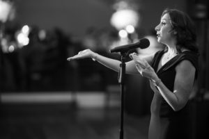 A woman singing into a microphone at a wedding in New York.