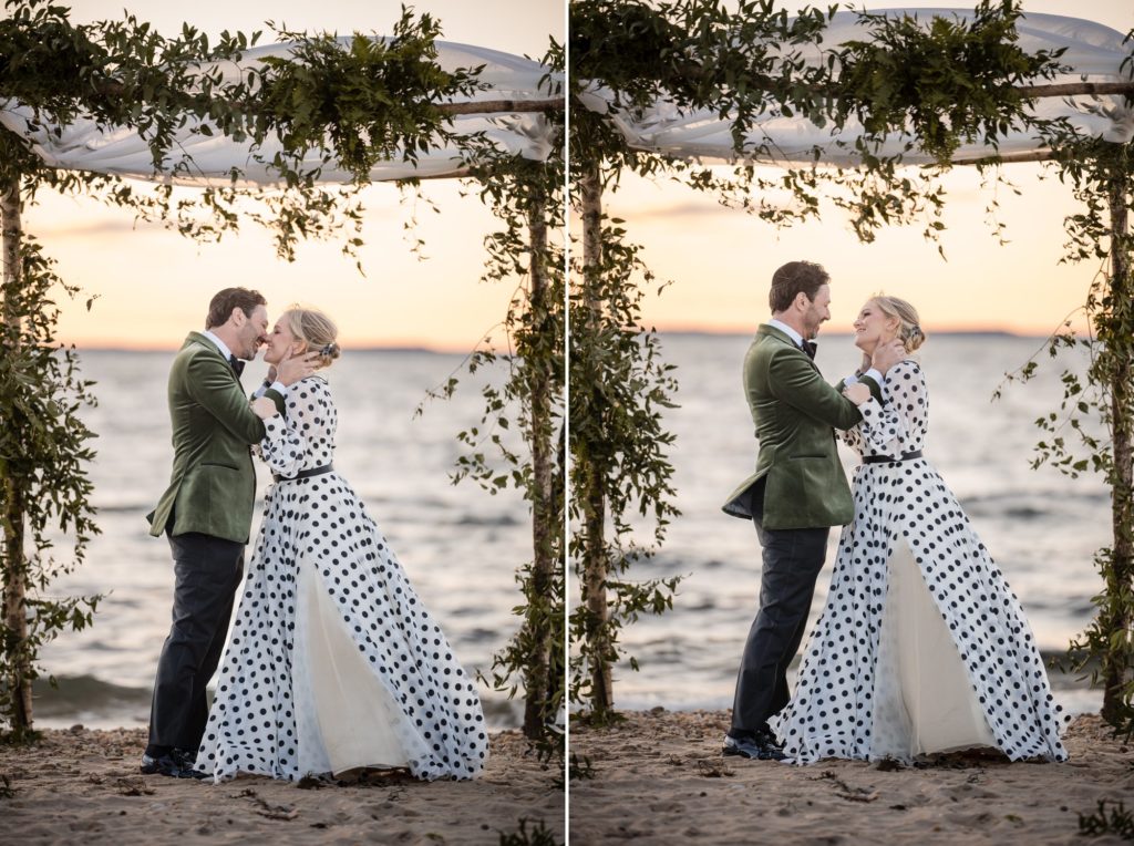 A bride and groom kiss under a polka dot arch on the beach in New York during their wedding ceremony.