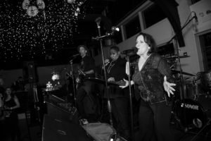 A black and white photo of a group of people singing on stage at a wedding in New York.