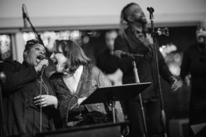Black and white photo of a woman singing into a microphone at a wedding in New York.