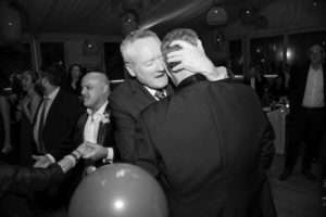 A black and white photo of two men hugging at a party in New York.