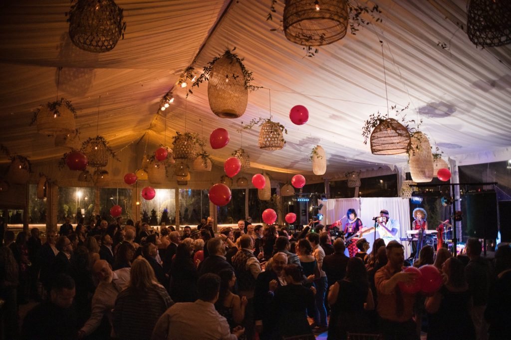 A crowd of people in a wedding tent with red balloons.