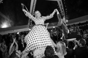 A woman in a polka dot dress is being held up by a group of people at a wedding in New York.