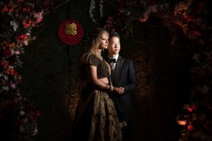 A bride and groom posing in front of a floral arch at their New York wedding.