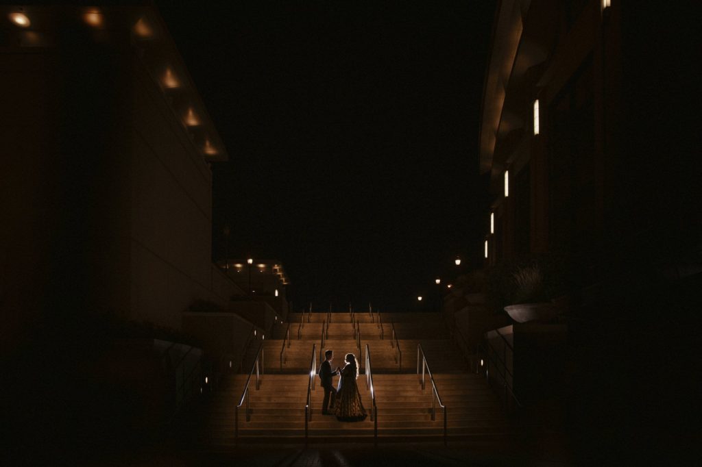 A bride and groom standing on stairs at night, captured during their magnificent wedding ceremony in New York.