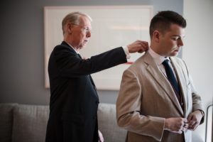 A man in New York helping another man put on a tie for a wedding.