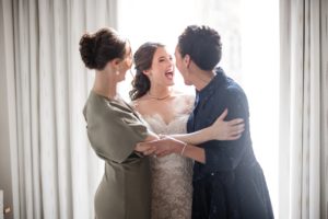 A bride and her bridesmaids hugging in front of a window in New York City during their wedding.