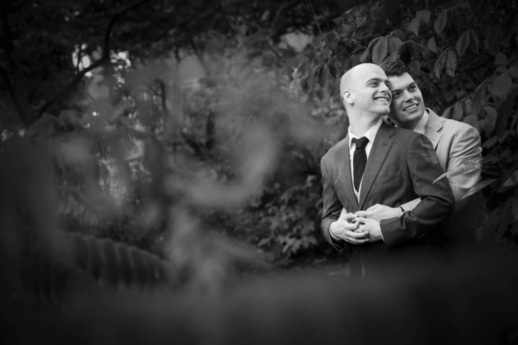 A black and white photo of two men hugging in the woods during their wedding in New York.