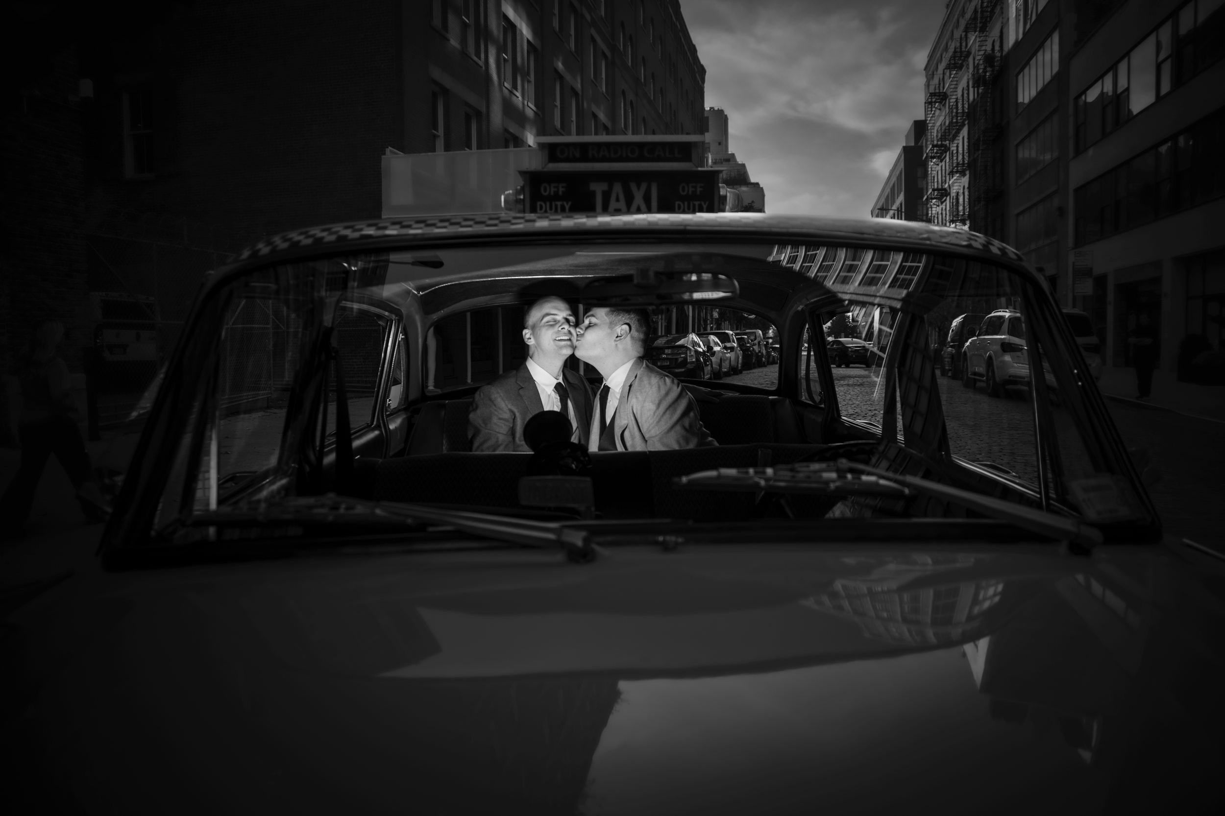 Two grooms in a black and white portrait in a vintage NYC taxicab