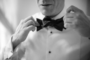 Black and white photo of a man putting on a bow tie for a wedding in New York.