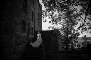A bride is standing on the steps of a castle in New York on her wedding day.