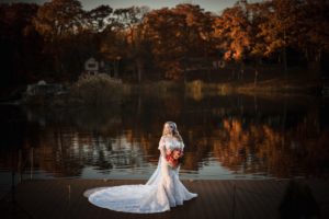 A bride standing on a dock in front of a lake at her New York wedding.