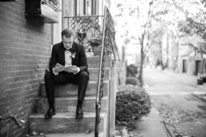 A groom reading a book on the steps of a building in New York City.