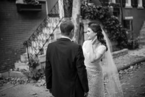A bride and groom share a loving glance at their wedding in front of a brick building in New York.