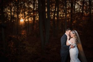 A bride and groom embrace in the woods at sunset during their New York wedding.
