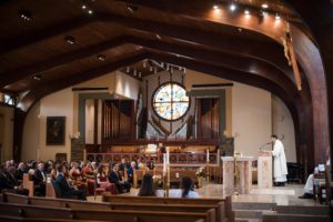 A wedding ceremony in a church in New York with a priest at the podium.