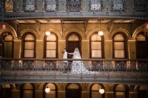 A bride and groom standing on the balcony of an ornate building in New York during their wedding.
