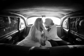 A bride and groom share a romantic kiss in the back seat of a car during their wedding in New York.