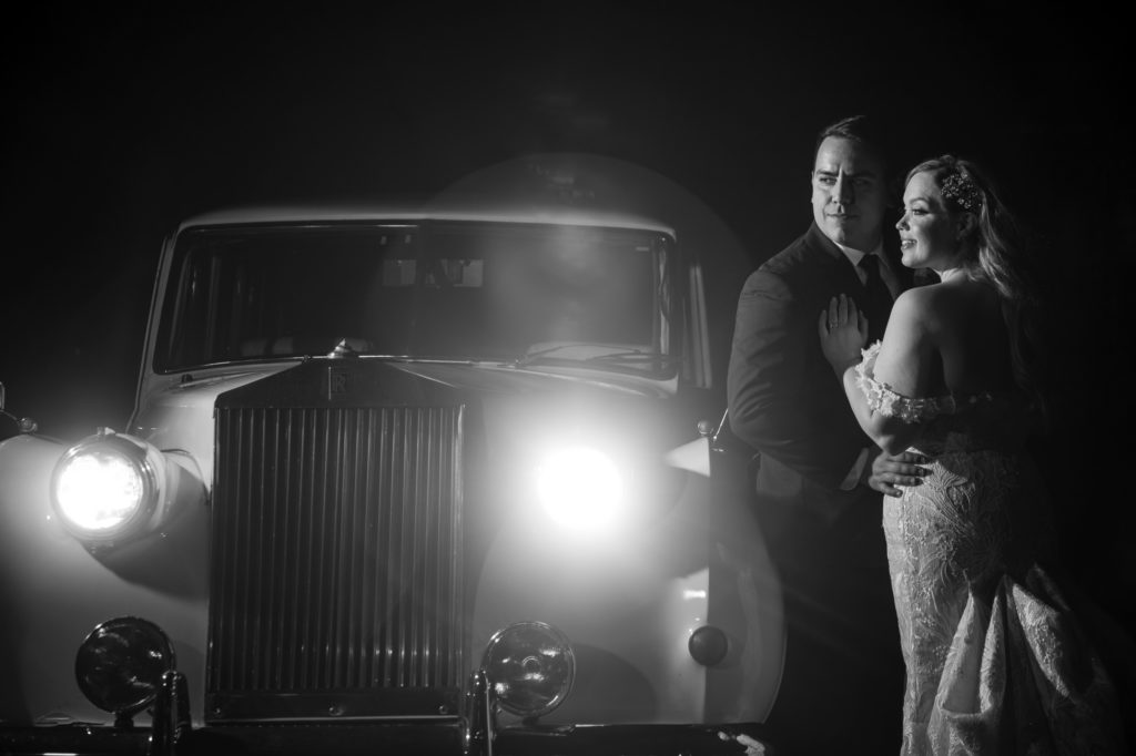 A bride and groom pose next to a vintage car at night in New York City for their wedding.